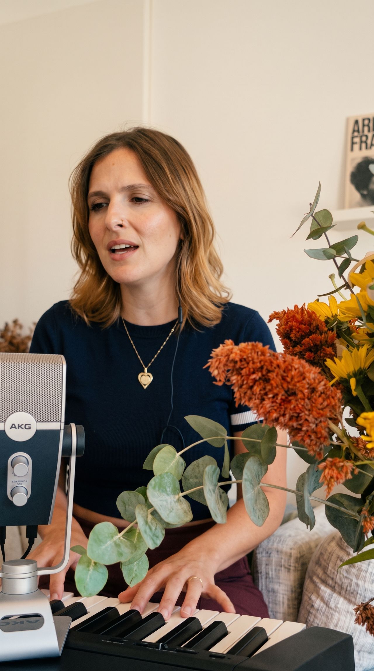 גל אילון שרה ומנגנת בקלידים בסטודיו, לצד מיקרופון אולפני ופרחים