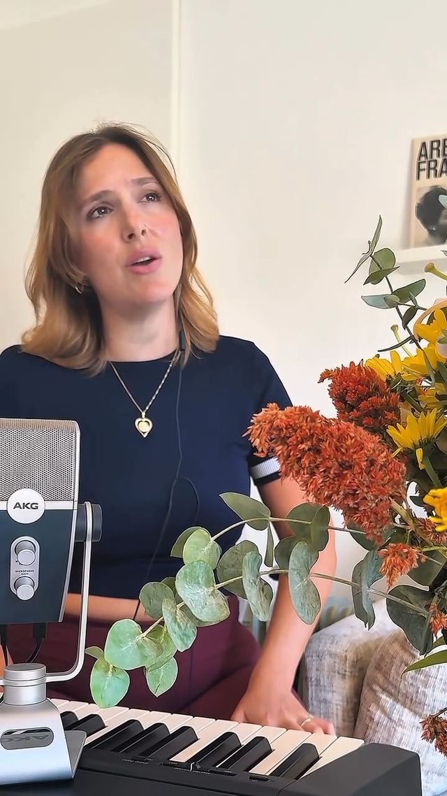 גל אילון שרה ומנגנת בקלידים בסטודיו, לצד מיקרופון אולפני ופרחים